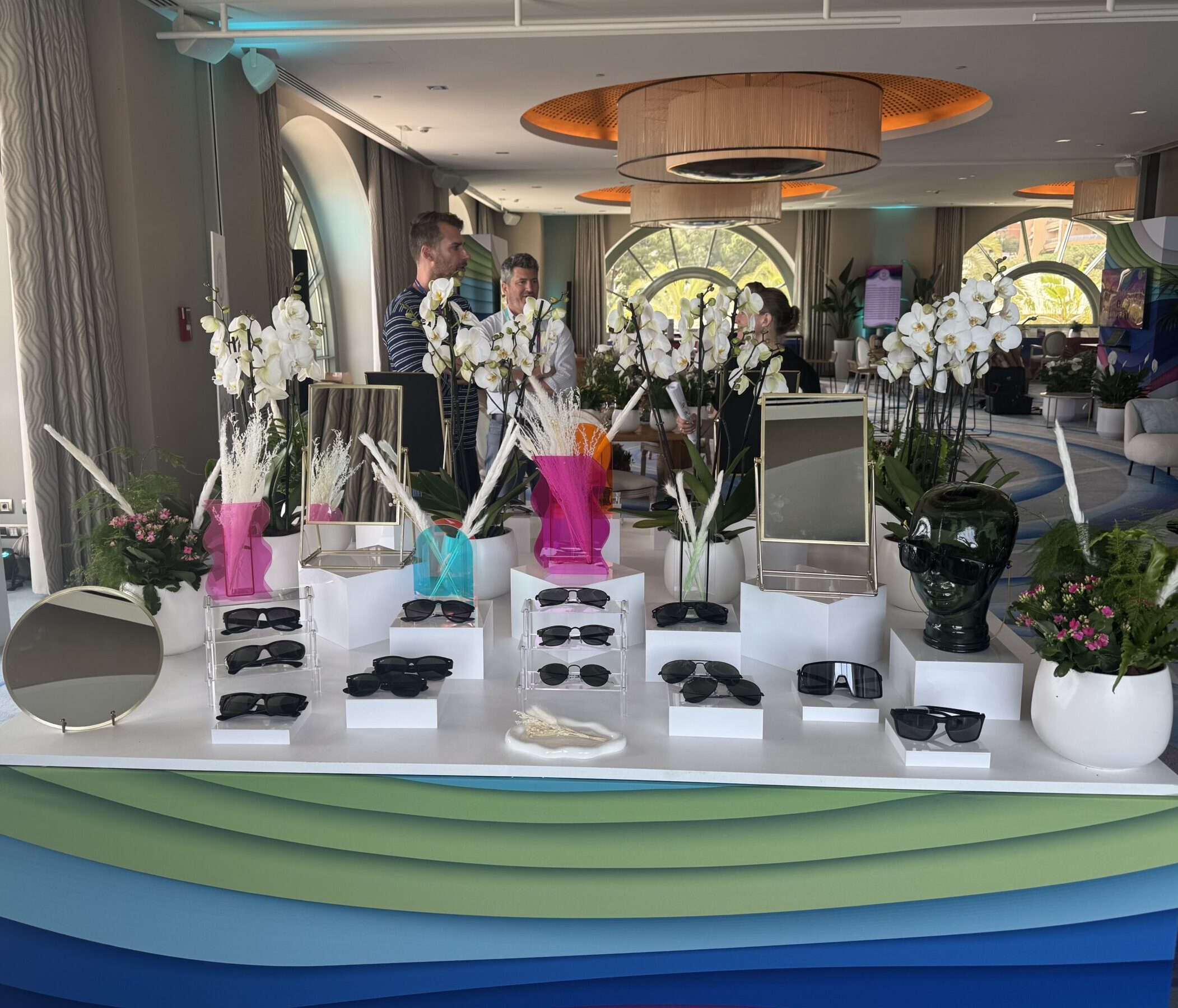 Guests at a corporate event stand behind a table of sunglasses available for selection.