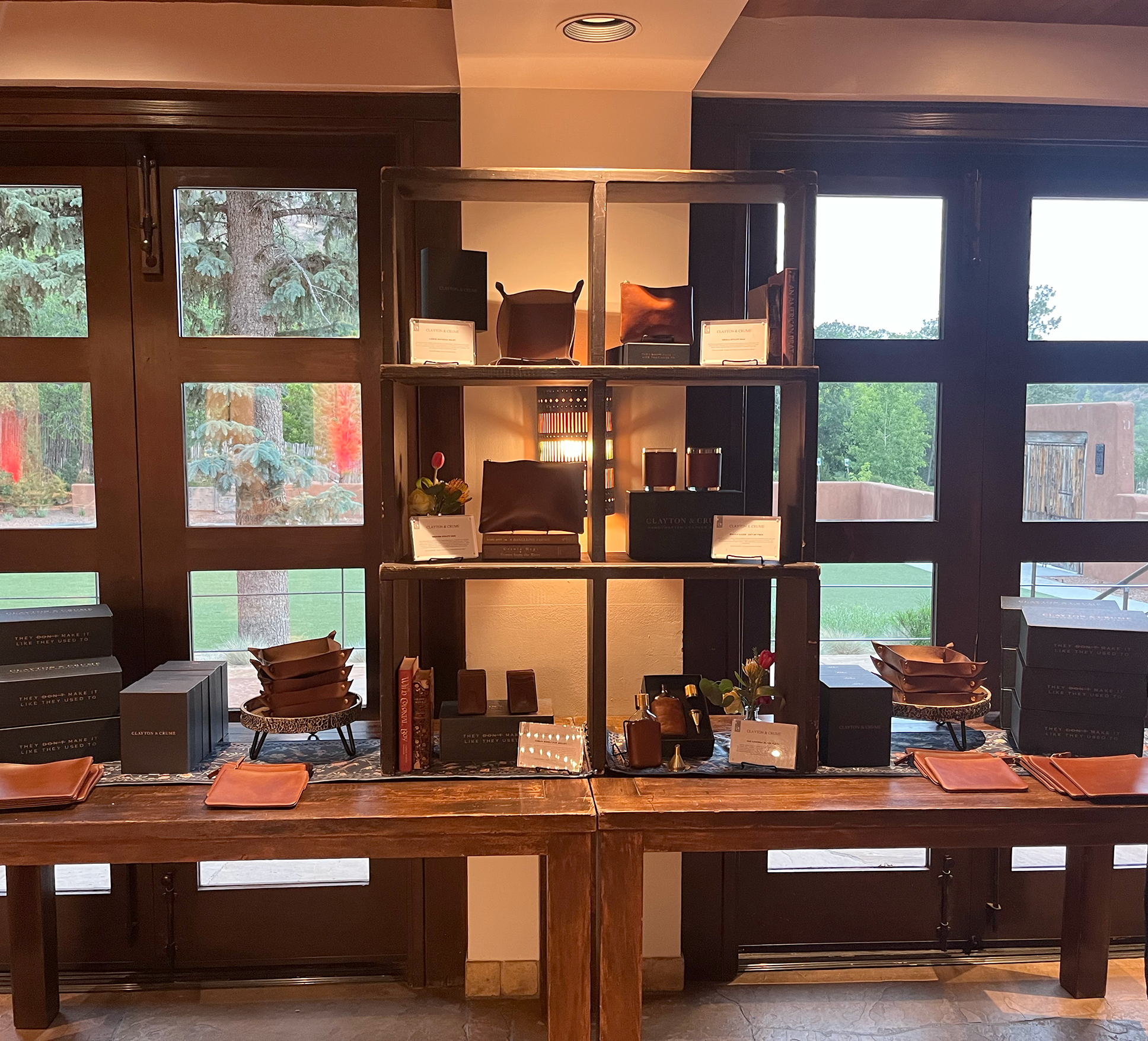 Leather Products courtesy of Clayton and Crume are displayed at an event in Santa Fe, NM. They are on a long table that offers shelving in the center.