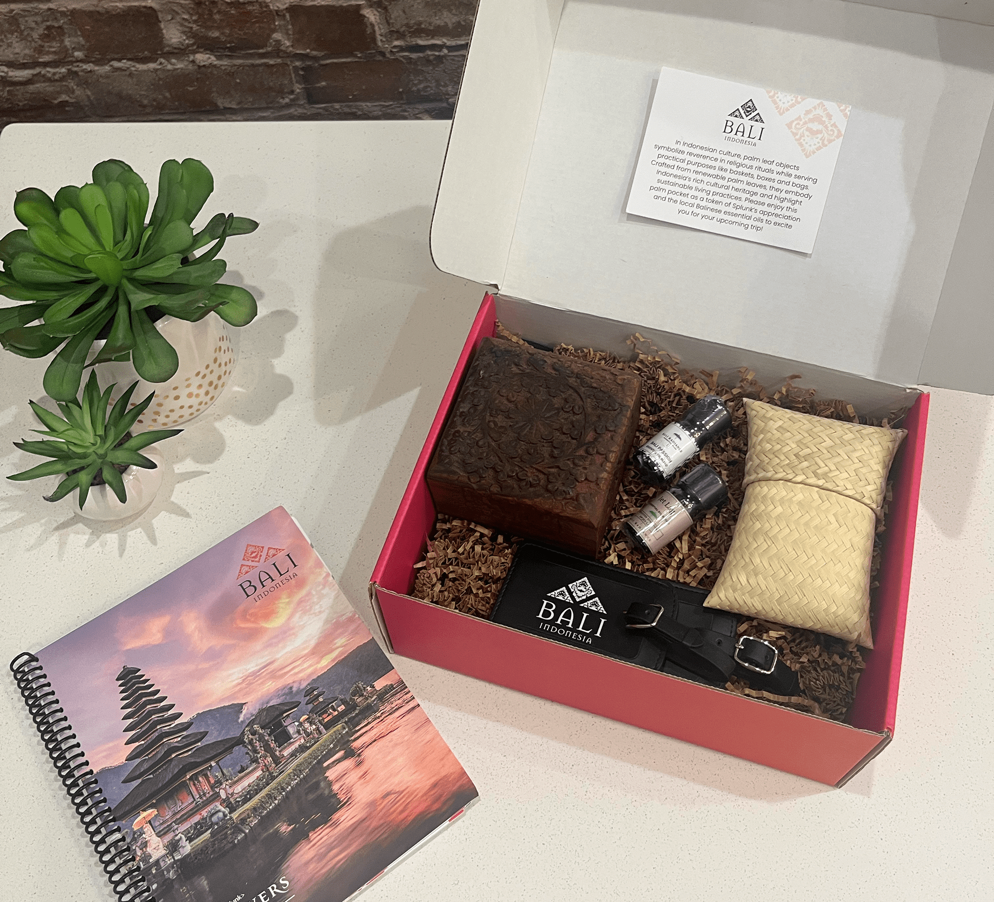 Pink box site next to matching coil bound booklet. Box has various small items including essential oils, trinket box and luggage tag.